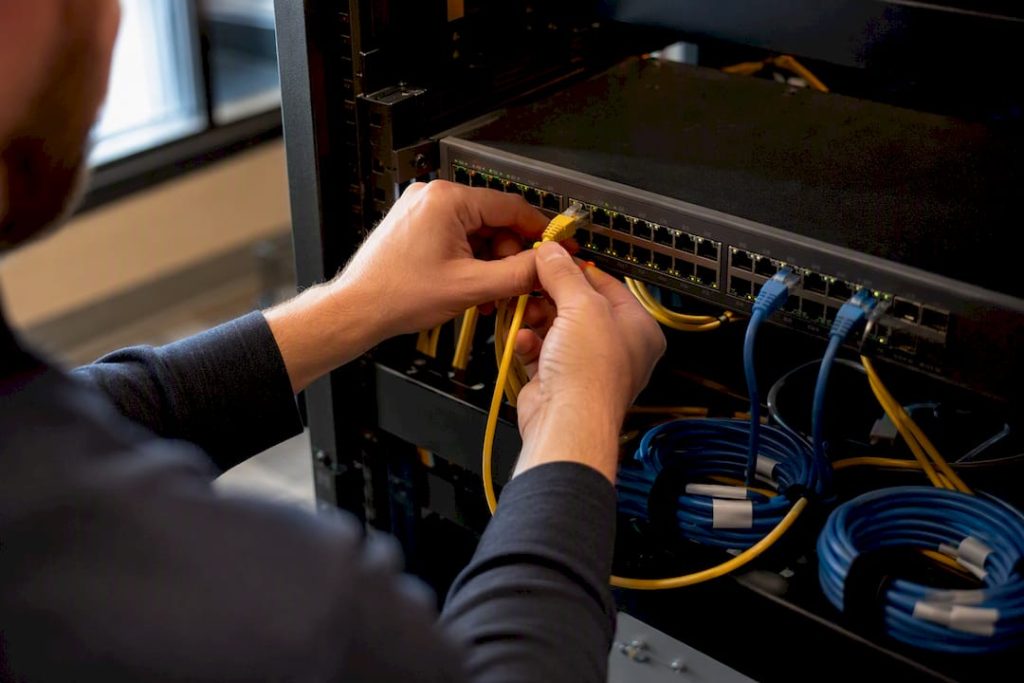 Hands connecting Ethernet cable to PoE switch